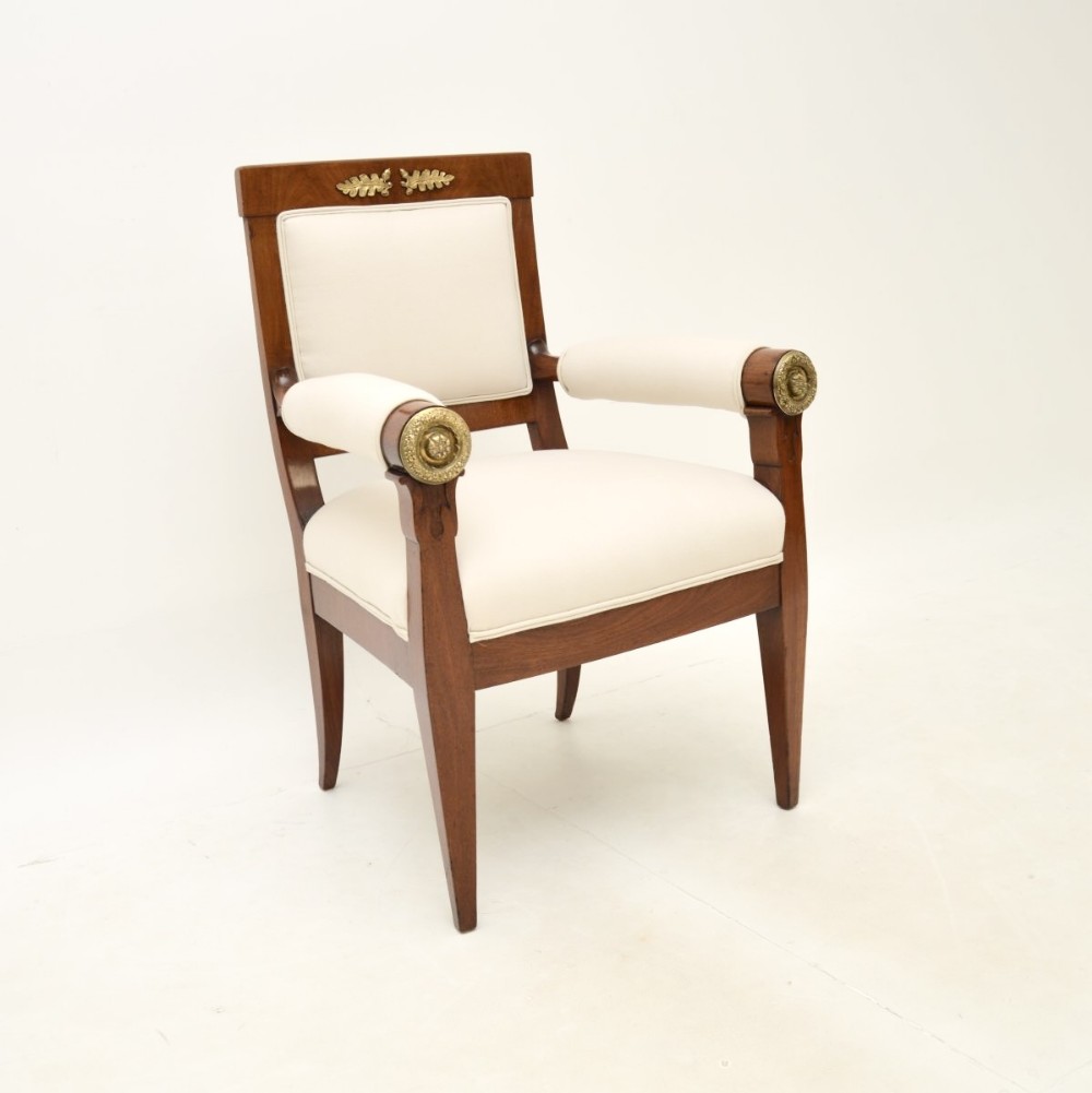 An antique Regency mahogany armchair with cream upholstered backrest, seat, and arm pads, featuring decorative brass mounts.
