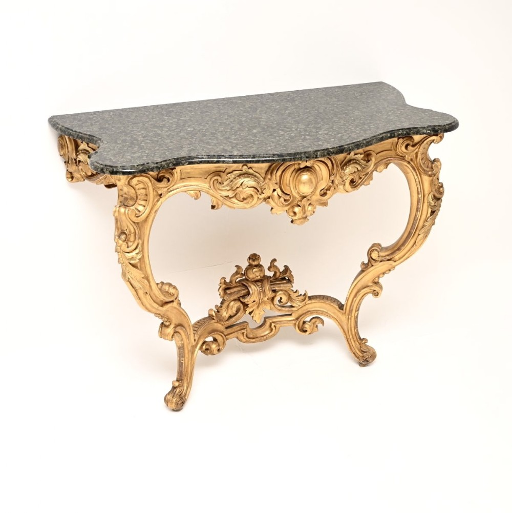 An antique French Rococo console table featuring a carved giltwood frame with cabriole legs and a dark green marble top.
