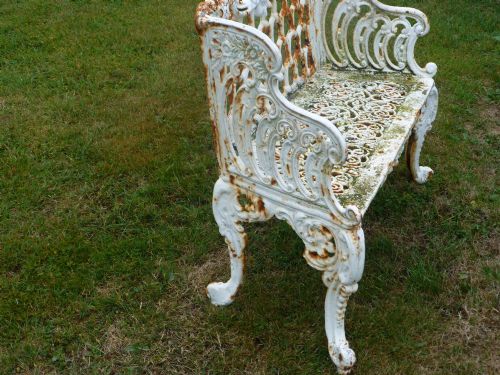 fig 2. A Victorian white painted cast iron garden bench displaying an ornate latticework backrest, scrolled armrests, pierced seat pattern, and areas of rust patination.