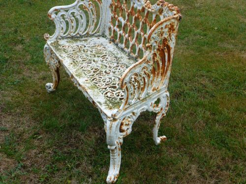 fig 3. A Victorian white painted cast iron garden bench displaying an ornate latticework backrest, scrolled armrests, pierced seat pattern, and areas of rust patination.