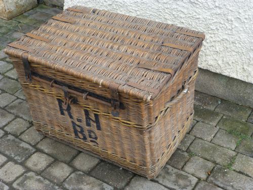 fig 1. A large 19th-century woven brown wicker travelling trunk with iron latches and stencilled black lettering on the front.