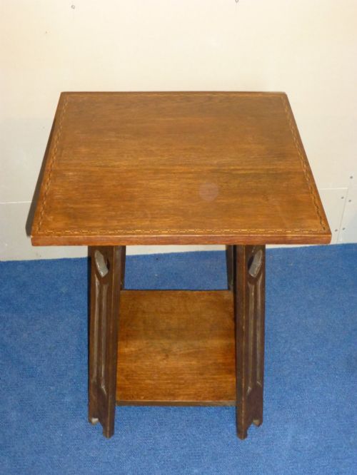 fig 1. An Arts and Crafts solid oak occasional table featuring a square top with fine chequered inlay, a lower shelf, and vertical leg supports with heart-shaped cutouts.
