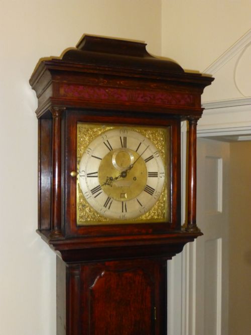 fig 3. An eighteenth-century dark oak and walnut longcase clock featuring a square brass dial, turned columns, and a hood with a moulded cornice.