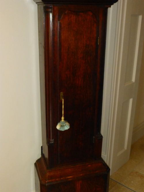 fig 4. An eighteenth-century dark oak and walnut longcase clock featuring a square brass dial, turned columns, and a hood with a moulded cornice.