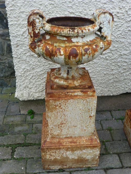 fig 1. A pair of Regency period cast iron campana urns with scrolled handles, displaying distressed off-white paint and surface rust, mounted on square cast iron pedestals.