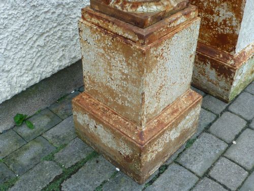 fig 3. A pair of Regency period cast iron campana urns with scrolled handles, displaying distressed off-white paint and surface rust, mounted on square cast iron pedestals.