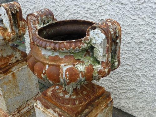 fig 4. A pair of Regency period cast iron campana urns with scrolled handles, displaying distressed off-white paint and surface rust, mounted on square cast iron pedestals.