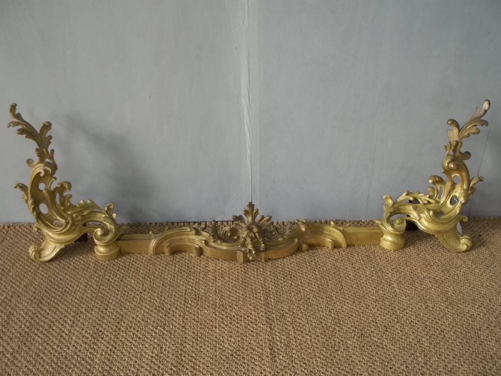 A 19th-century gilt bronze Rococo fireplace fender featuring adjustable scrolling acanthus leaf chenets at each end.