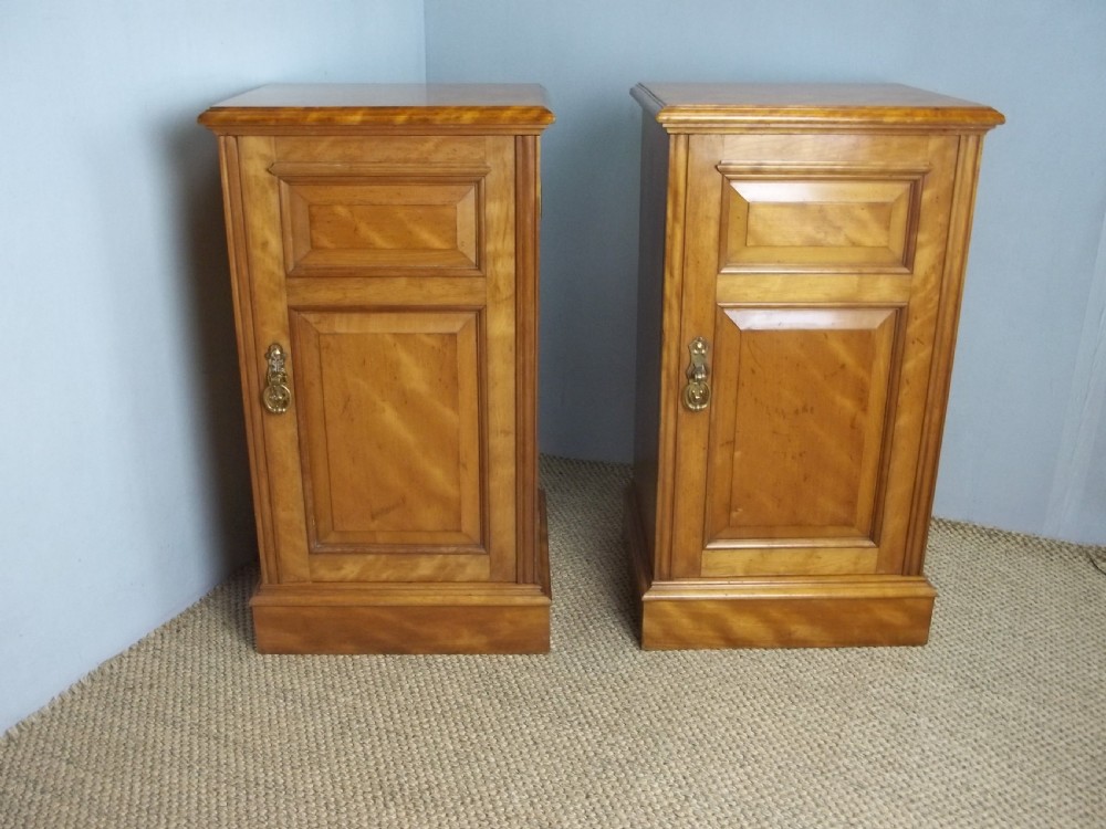 A matching pair of late 19th-century English satin birch bedside cupboards with panelled single doors, brass handles, and plinth bases.