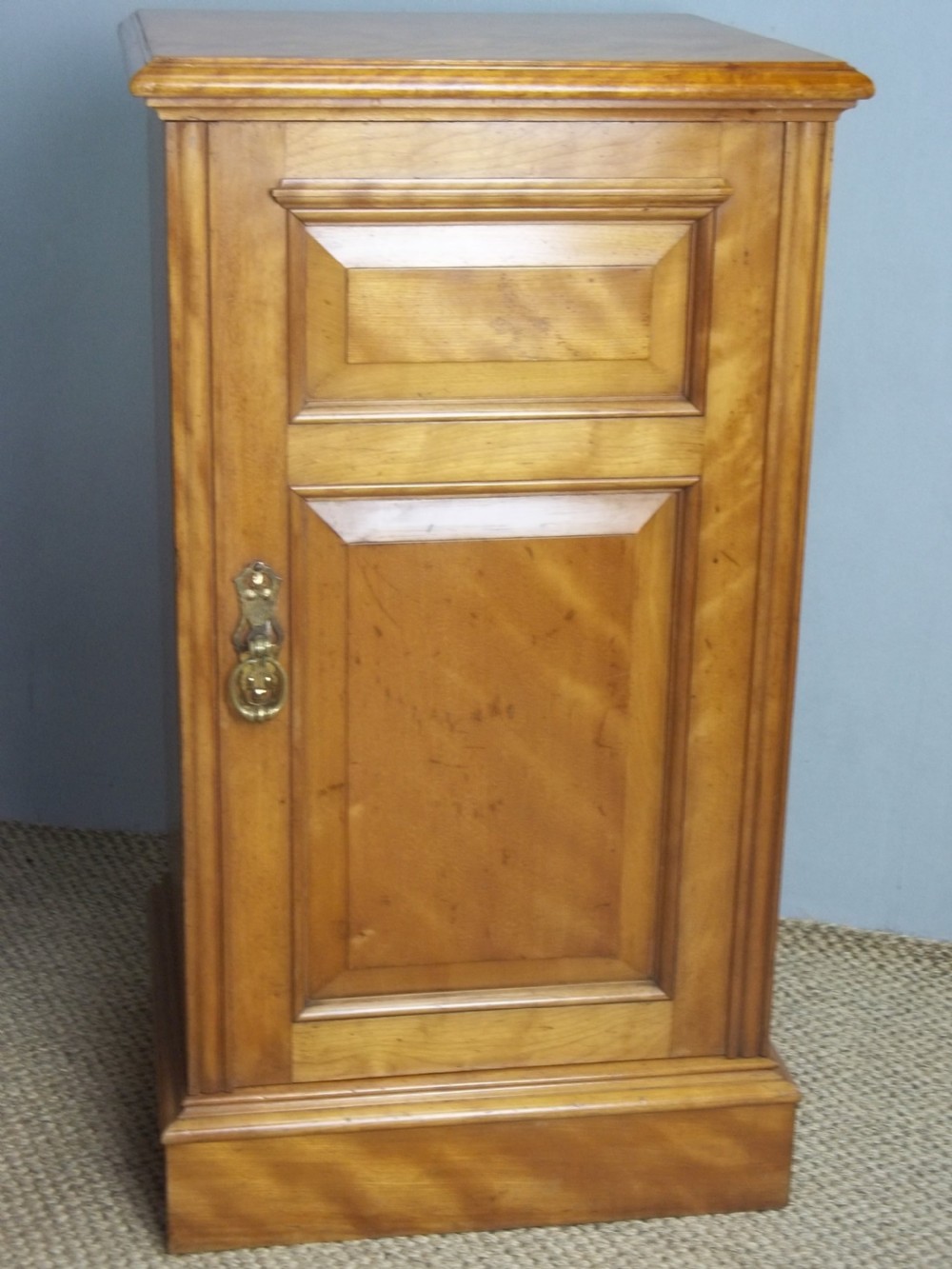 A matching pair of late 19th-century English satin birch bedside cupboards with panelled single doors, brass handles, and plinth bases. View II