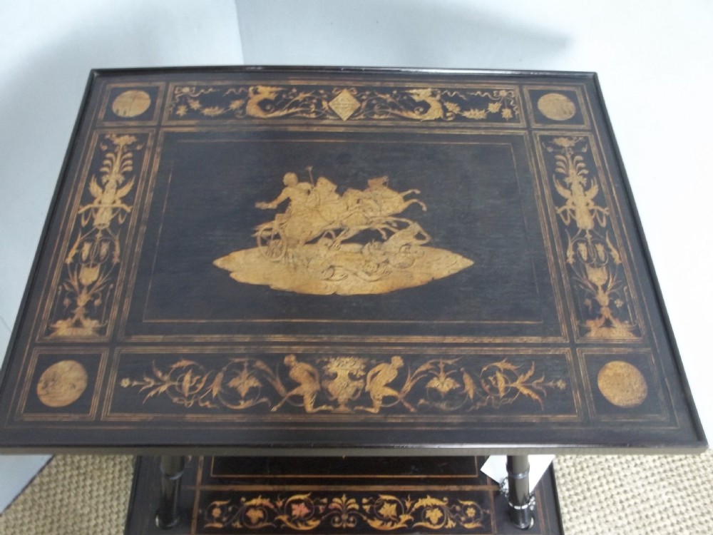 An ebonised two-tier side table displaying Sorrento marquetry inlay depicting a central chariot scene surrounded by decorative foliage and resting on turned legs. View II