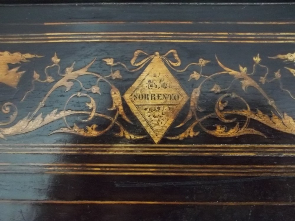 An ebonised two-tier side table displaying Sorrento marquetry inlay depicting a central chariot scene surrounded by decorative foliage and resting on turned legs. View III