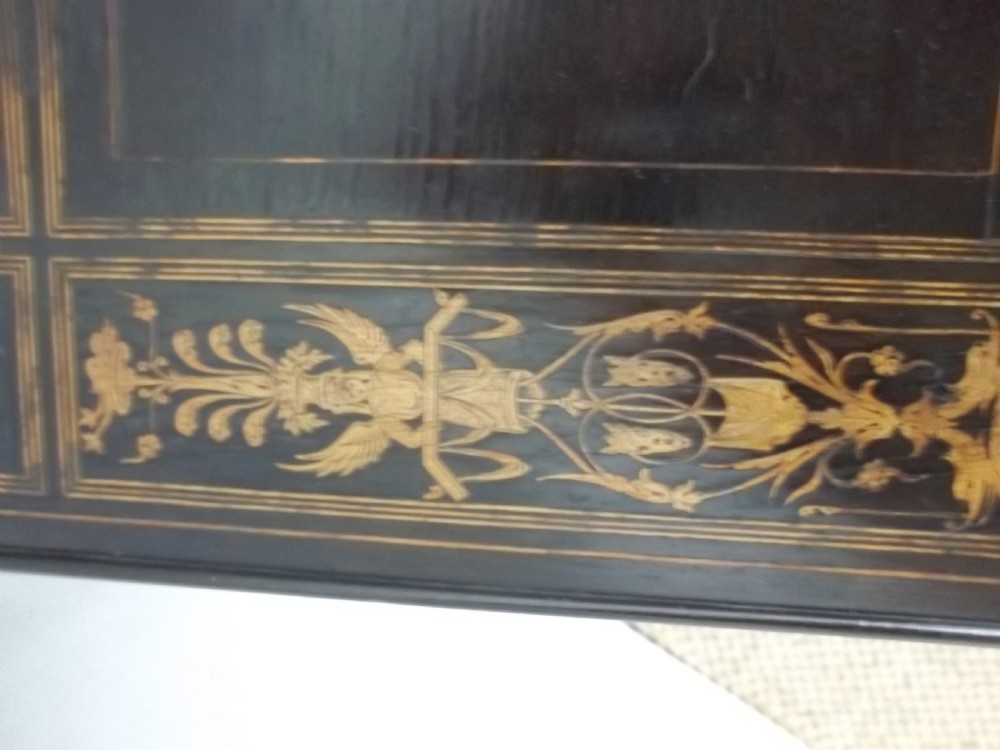 An ebonised two-tier side table displaying Sorrento marquetry inlay depicting a central chariot scene surrounded by decorative foliage and resting on turned legs. View VI
