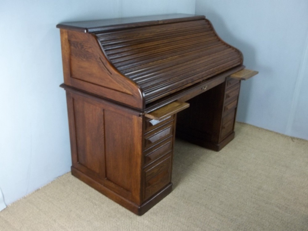 A large warm brown oak roll top pedestal desk featuring a slatted tambour front, twin pedestals with drawers, and pull-out writing slides.