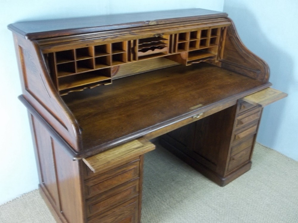 A large warm brown oak roll top pedestal desk featuring a slatted tambour front, twin pedestals with drawers, and pull-out writing slides. View II