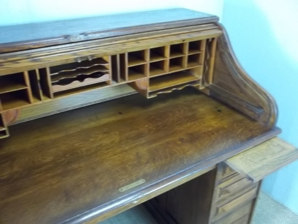 A large warm brown oak roll top pedestal desk featuring a slatted tambour front, twin pedestals with drawers, and pull-out writing slides. View III