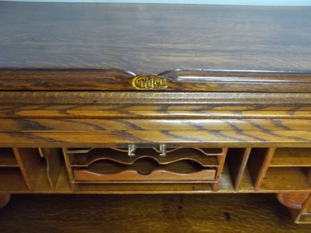 A large warm brown oak roll top pedestal desk featuring a slatted tambour front, twin pedestals with drawers, and pull-out writing slides. View V