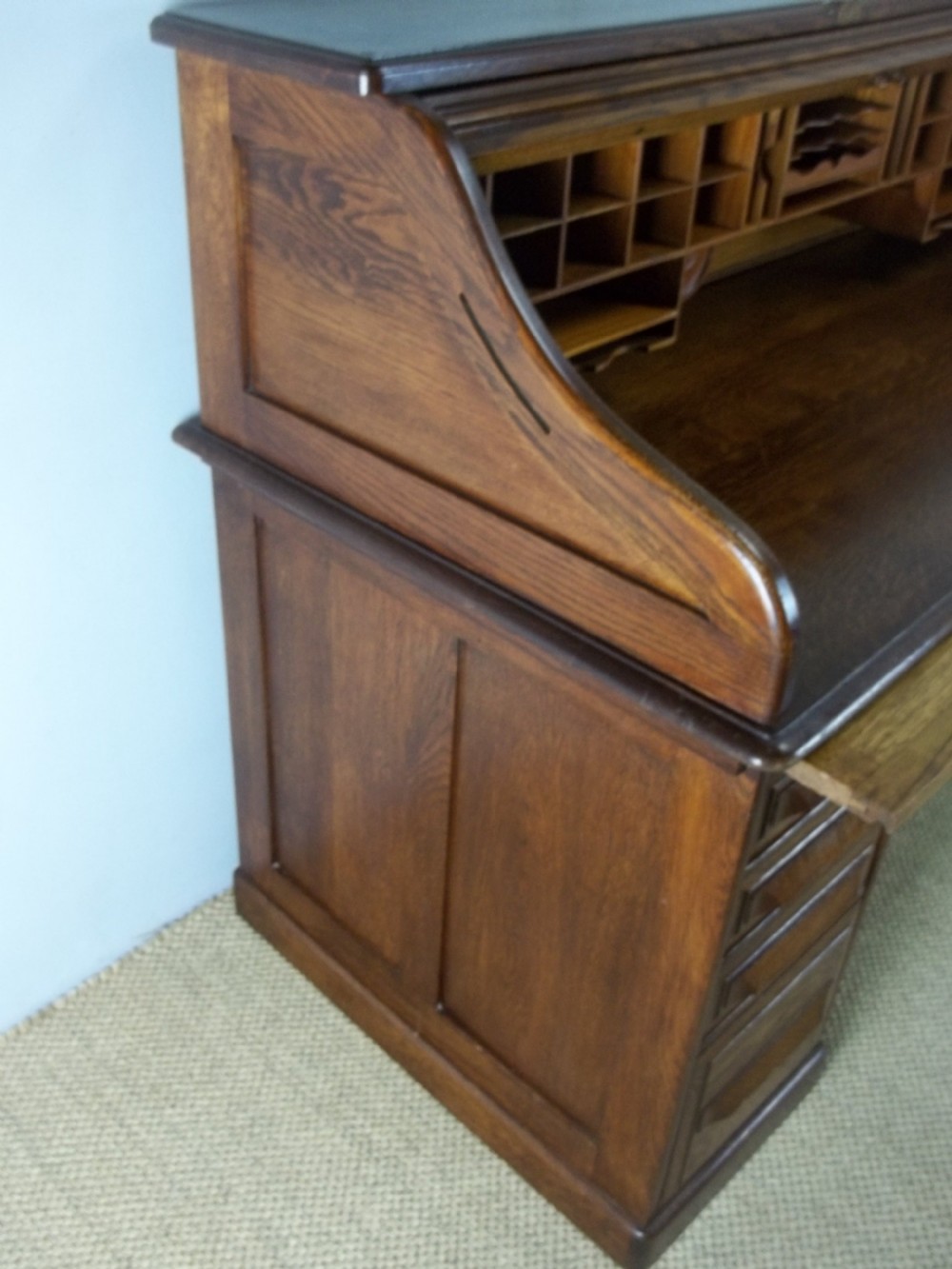 A large warm brown oak roll top pedestal desk featuring a slatted tambour front, twin pedestals with drawers, and pull-out writing slides. View VI