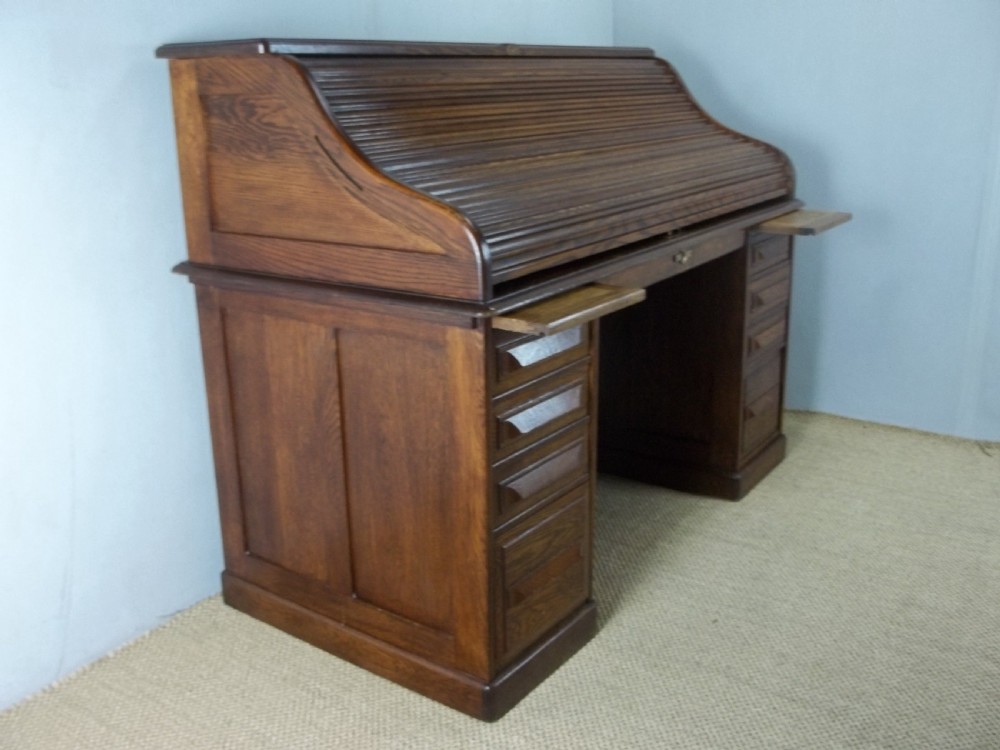 A large warm brown oak roll top pedestal desk featuring a slatted tambour front, twin pedestals with drawers, and pull-out writing slides. View VII