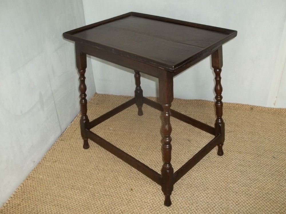 A dark brown oak side table featuring a tray top with a raised moulded rim, turned legs, and a low rectangular box stretcher base.