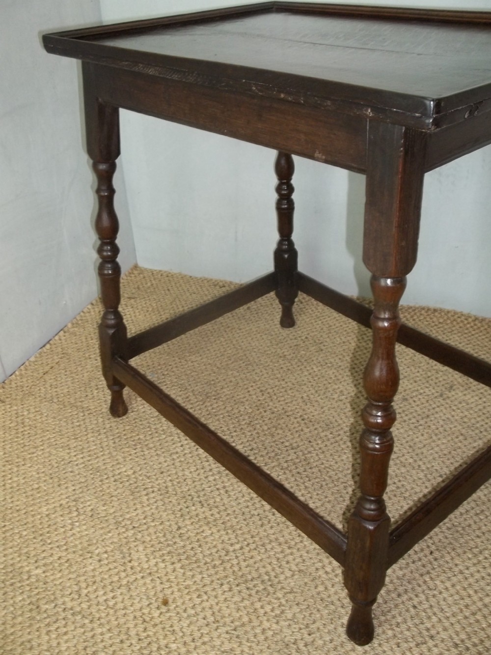 A dark brown oak side table featuring a tray top with a raised moulded rim, turned legs, and a low rectangular box stretcher base. View VII