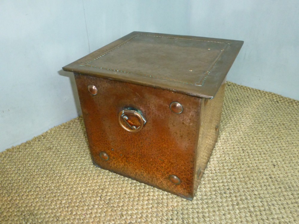 An Arts and Crafts copper square coal purdonium box featuring a planished surface, corner rivets, and drop ring handles.