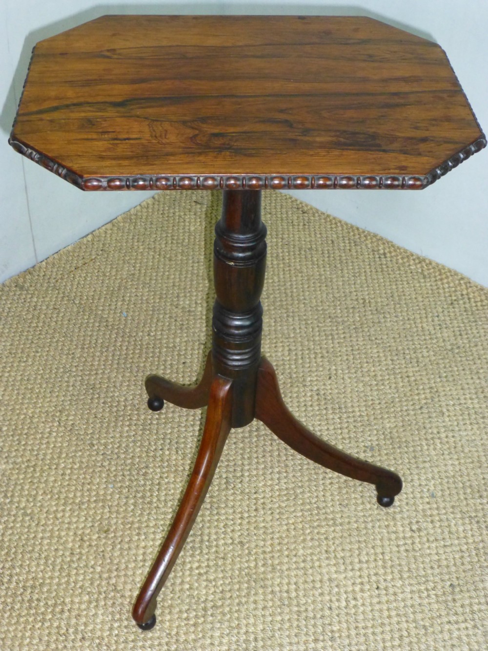 A Regency era rosewood occasional wine table featuring an octagonal top with beaded edging, a turned central pedestal, and three downswept tripod legs.