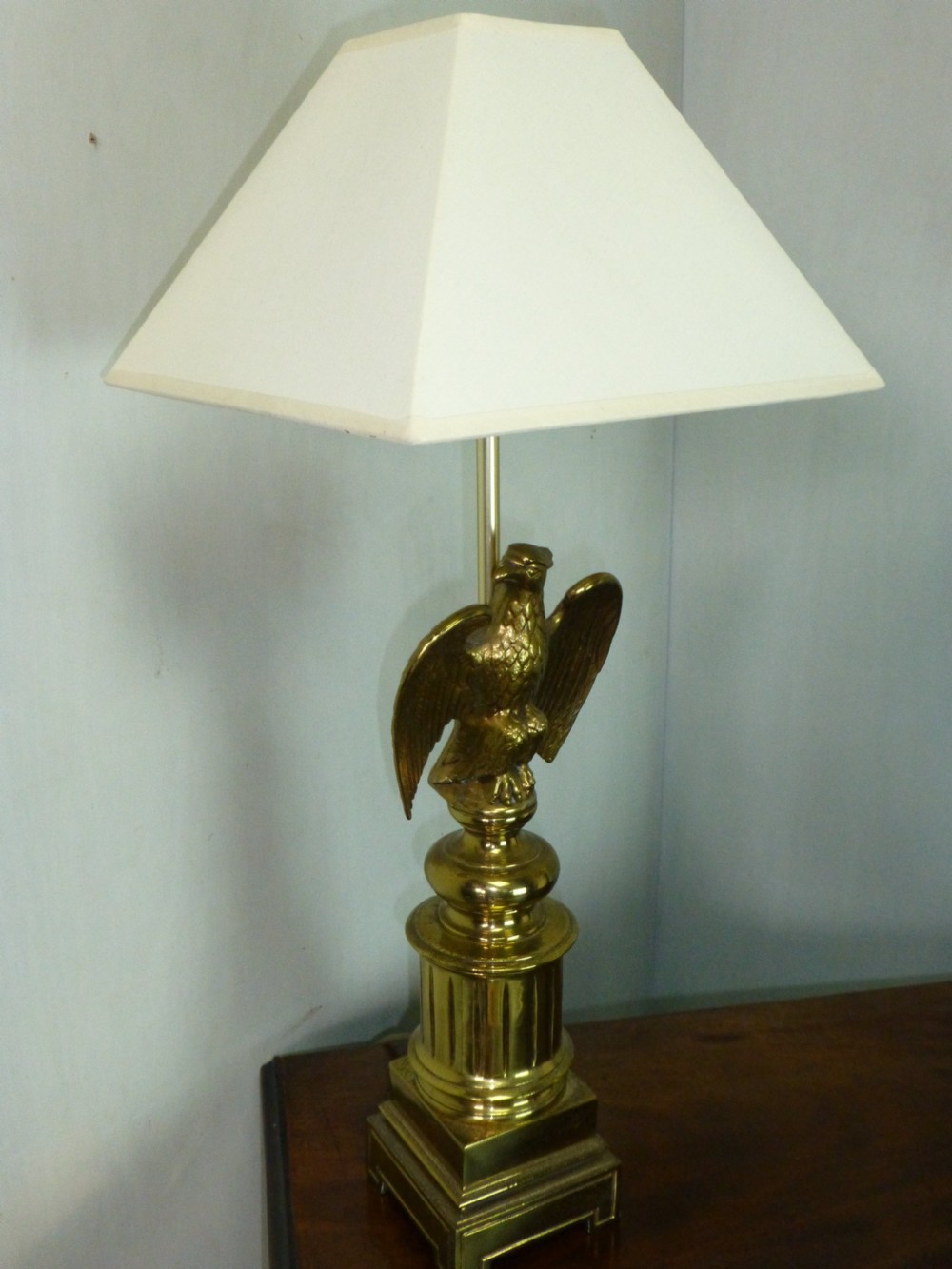 A pair of cast brass table lamps featuring eagle sculptures on stepped pedestal bases with cream pyramid shades. View II