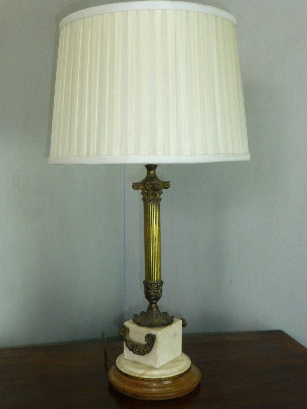 An antique Edwardian table lamp featuring a fluted brass column on a white marble plinth with a pleated cream shade.