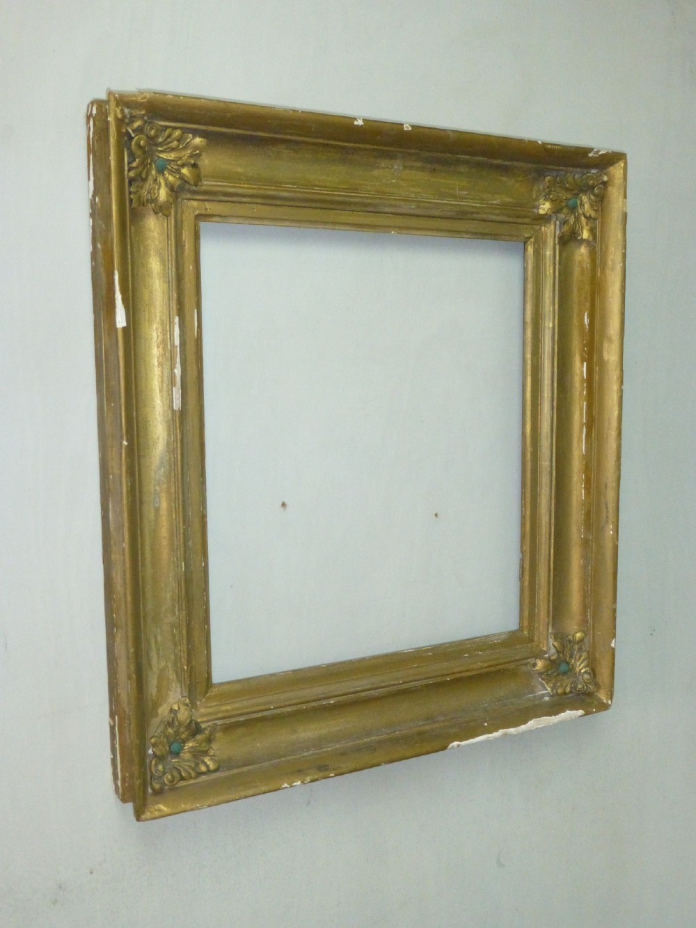 A square 19th-century giltwood frame featuring deep cove mouldings and carved acanthus leaf corner ornaments against a white wall.
