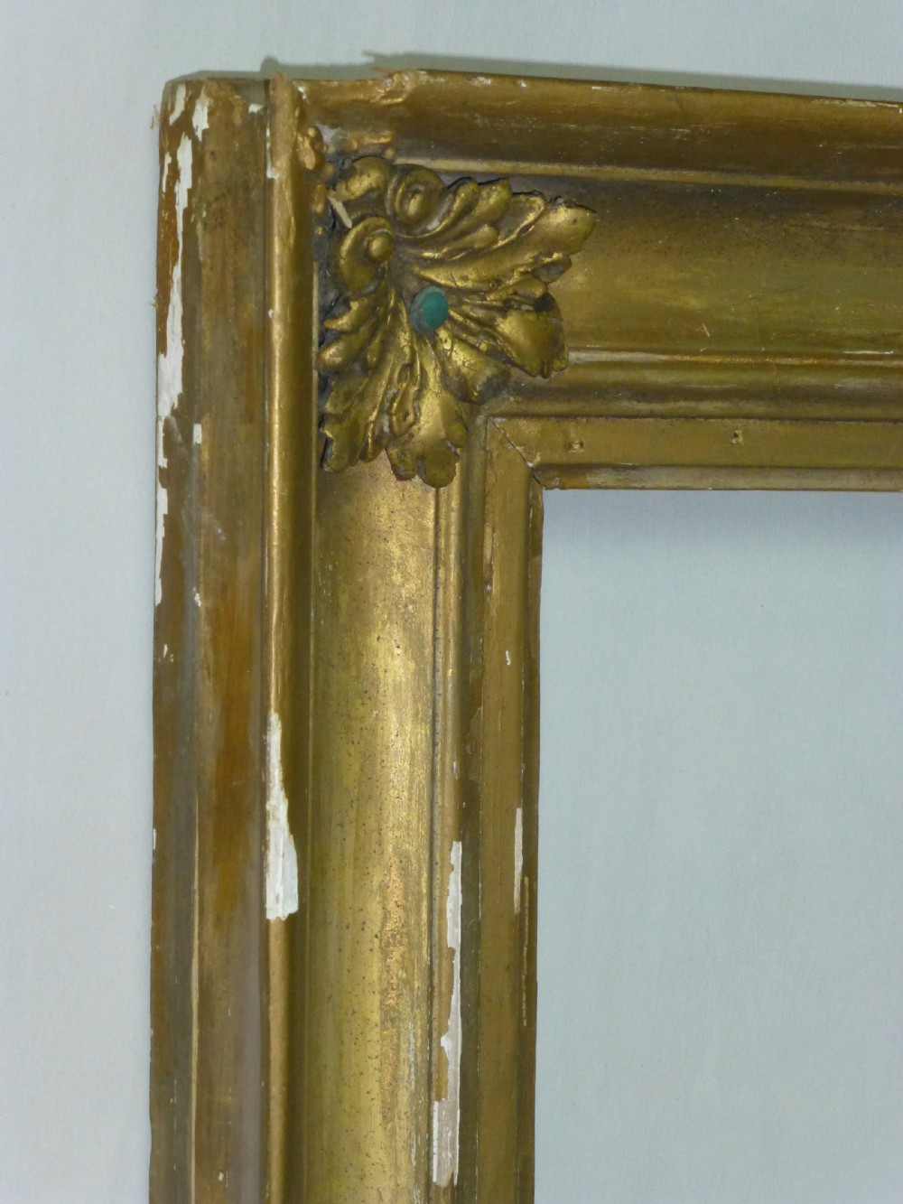 A square 19th-century giltwood frame featuring deep cove mouldings and carved acanthus leaf corner ornaments against a white wall. View II