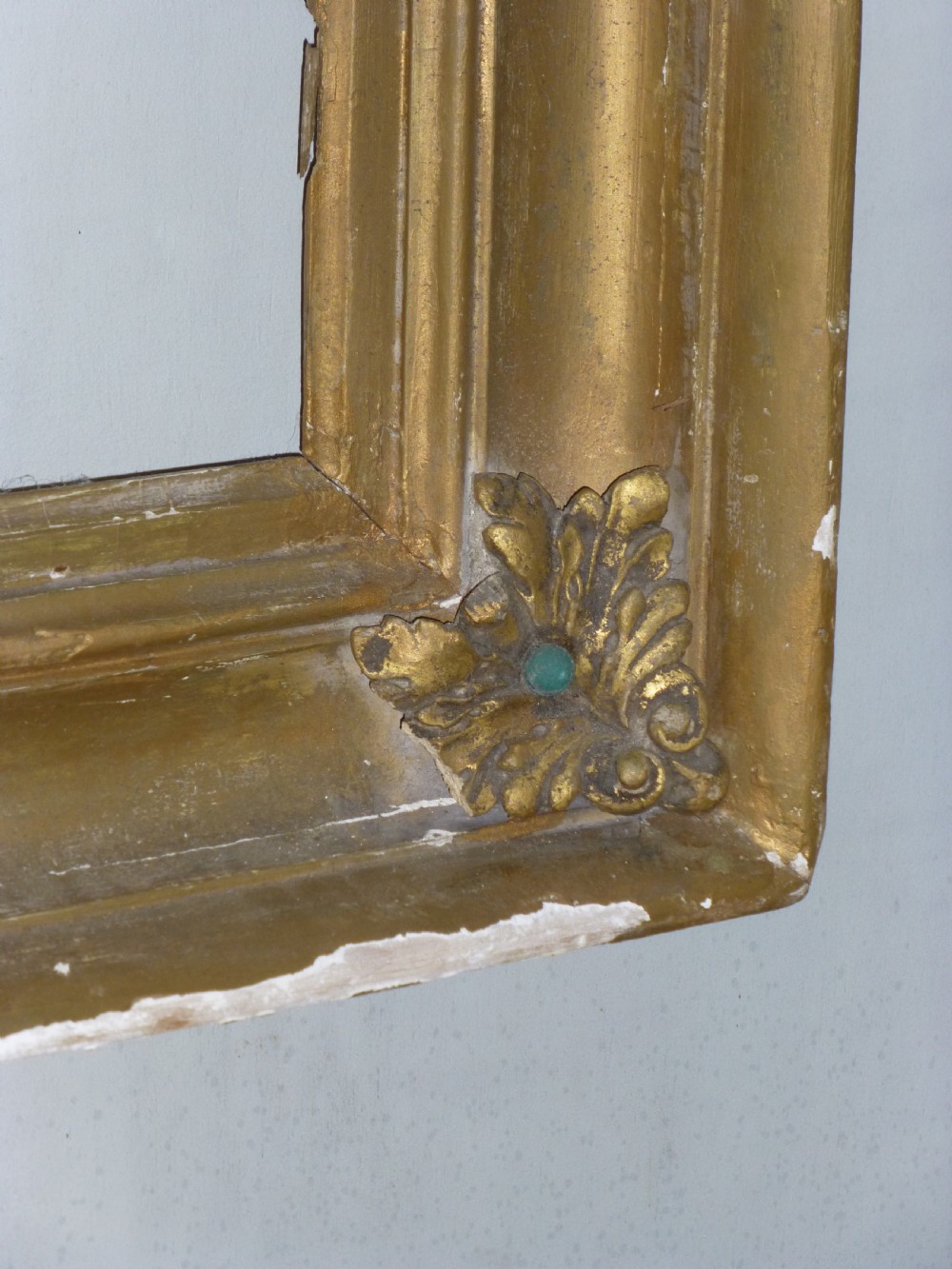 A square 19th-century giltwood frame featuring deep cove mouldings and carved acanthus leaf corner ornaments against a white wall. View IV
