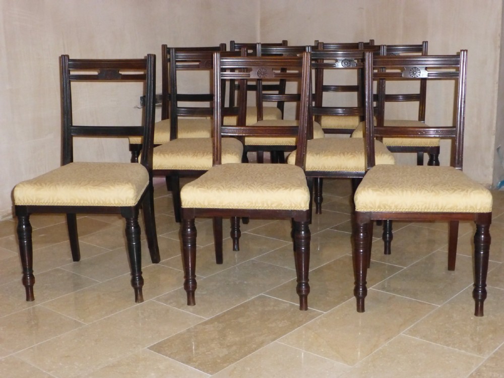 A set of ten 19th-century Victorian dark mahogany dining chairs featuring carved back rails, turned front legs, and yellow patterned fabric upholstered seats.