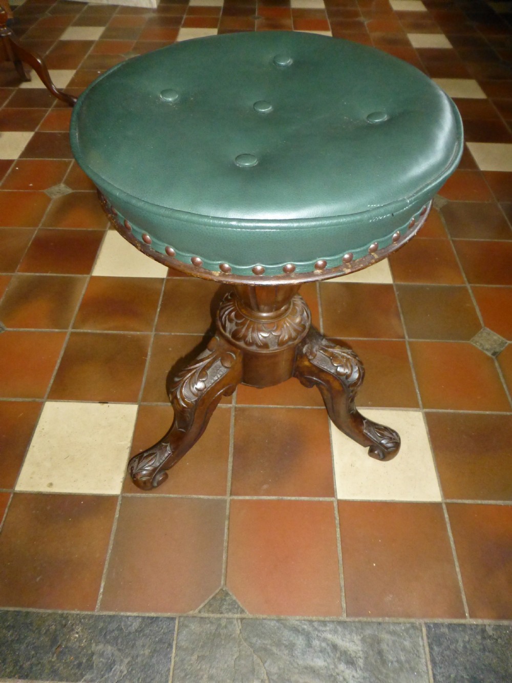 A 19th-century Victorian revolving piano stool featuring a deep green leather buttoned seat mounted on a carved walnut tripod base.