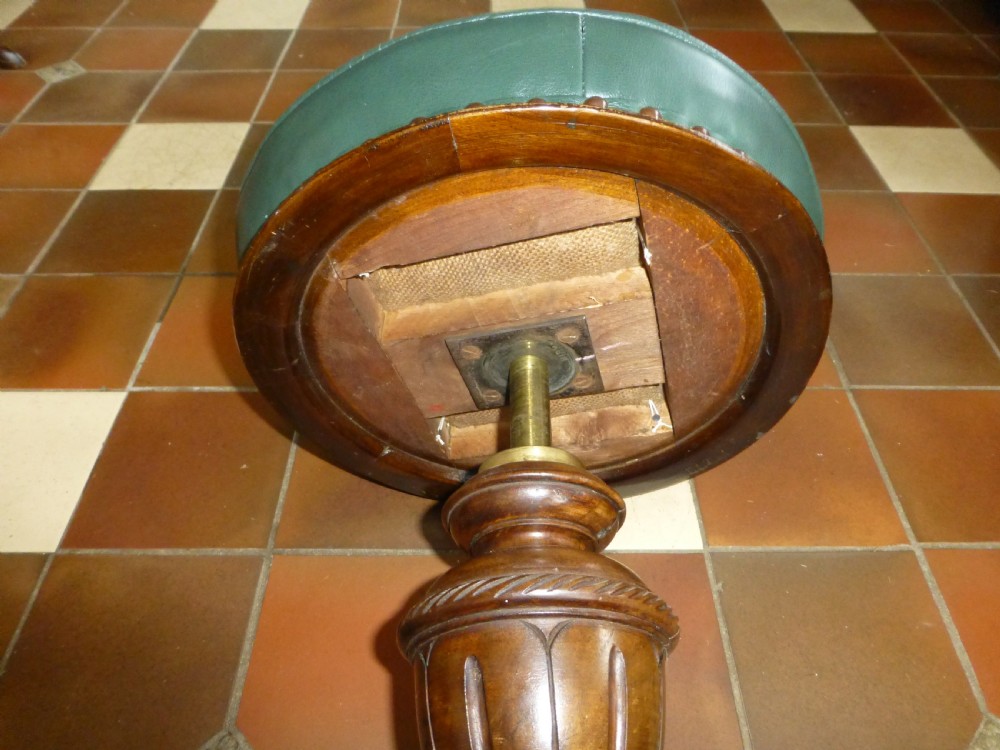 A 19th-century Victorian revolving piano stool featuring a deep green leather buttoned seat mounted on a carved walnut tripod base. View VI
