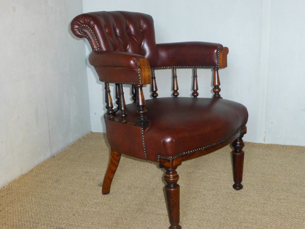 A Victorian oak captains desk chair with button-backed chestnut brown leather upholstery, turned spindles, and brass stud trim.