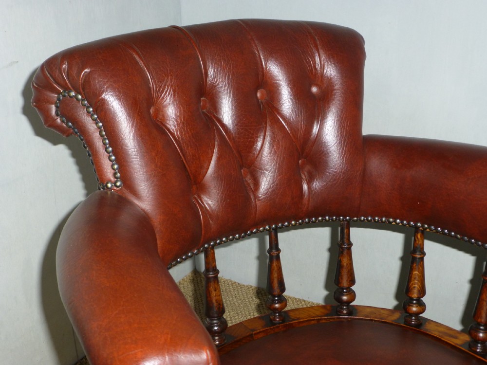 A Victorian oak captains desk chair with button-backed chestnut brown leather upholstery, turned spindles, and brass stud trim. View II