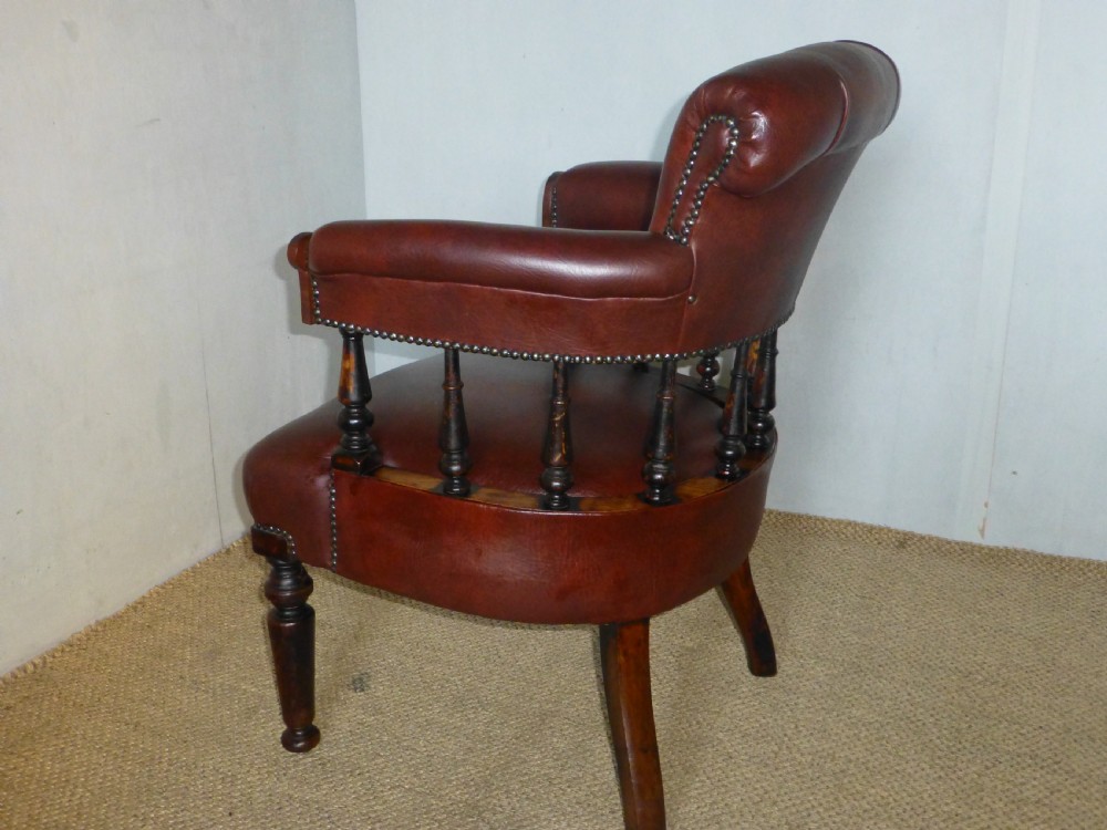 A Victorian oak captains desk chair with button-backed chestnut brown leather upholstery, turned spindles, and brass stud trim. View V
