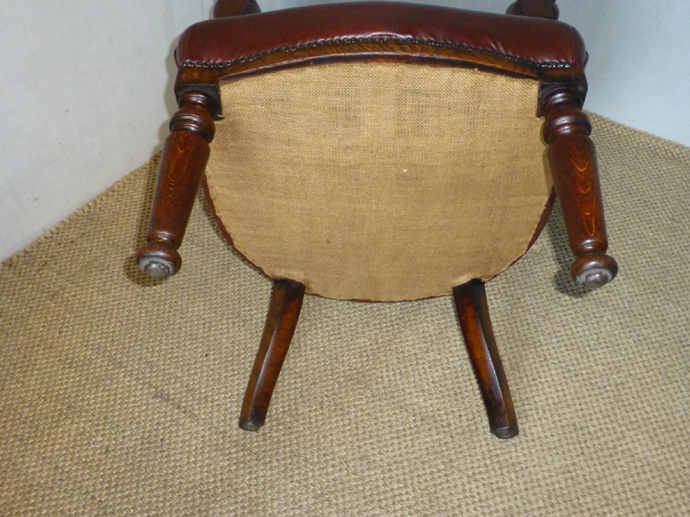A Victorian oak captains desk chair with button-backed chestnut brown leather upholstery, turned spindles, and brass stud trim. View VI