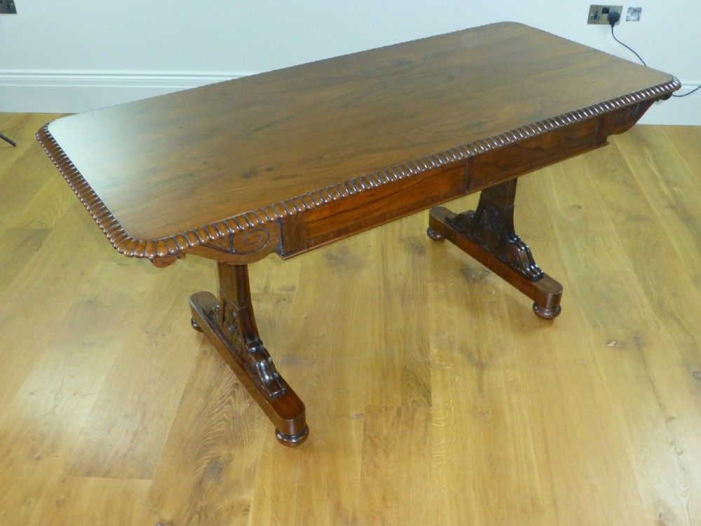 A Regency period rosewood writing table featuring a gadrooned top edge, frieze drawers, and carved trestle end supports.