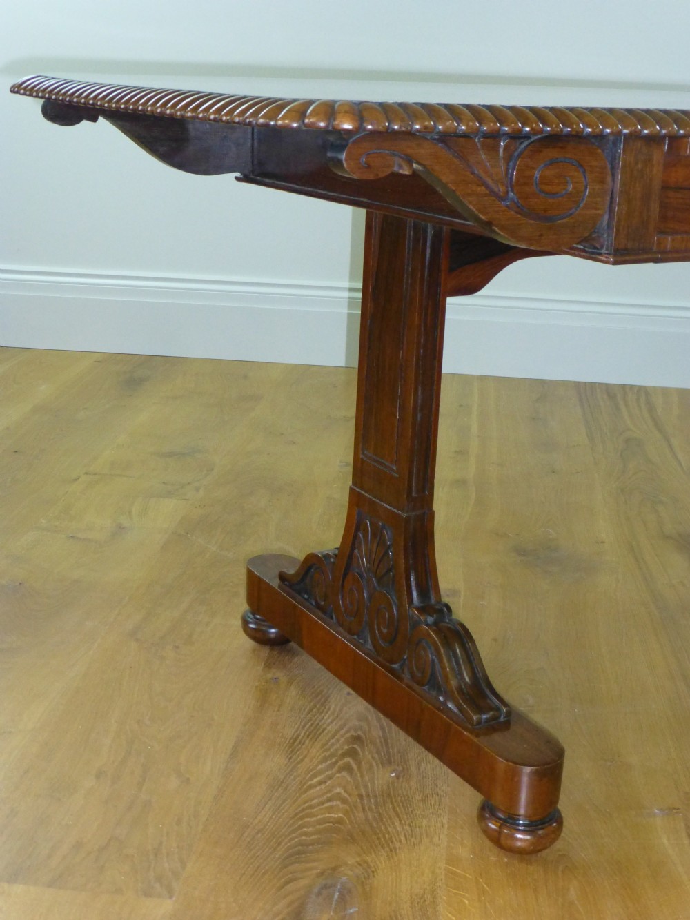 A Regency period rosewood writing table featuring a gadrooned top edge, frieze drawers, and carved trestle end supports. View II