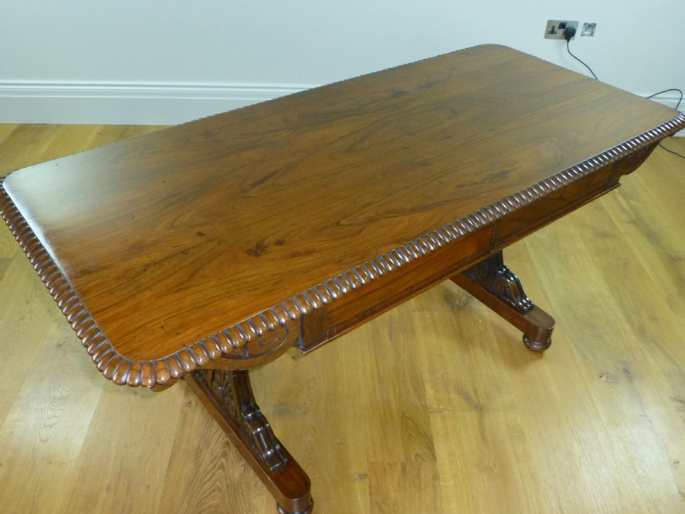 A Regency period rosewood writing table featuring a gadrooned top edge, frieze drawers, and carved trestle end supports. View III