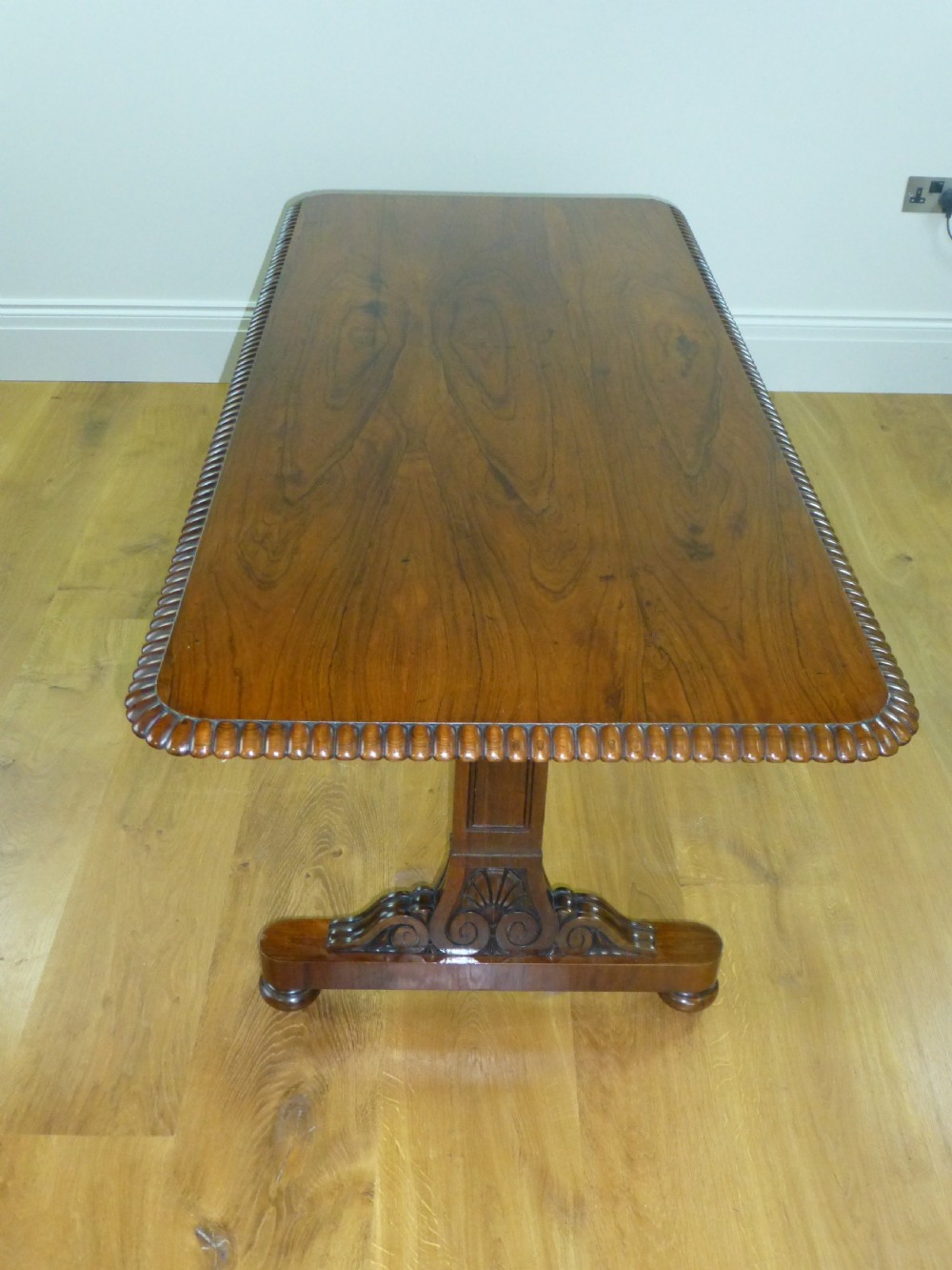 A Regency period rosewood writing table featuring a gadrooned top edge, frieze drawers, and carved trestle end supports. View V