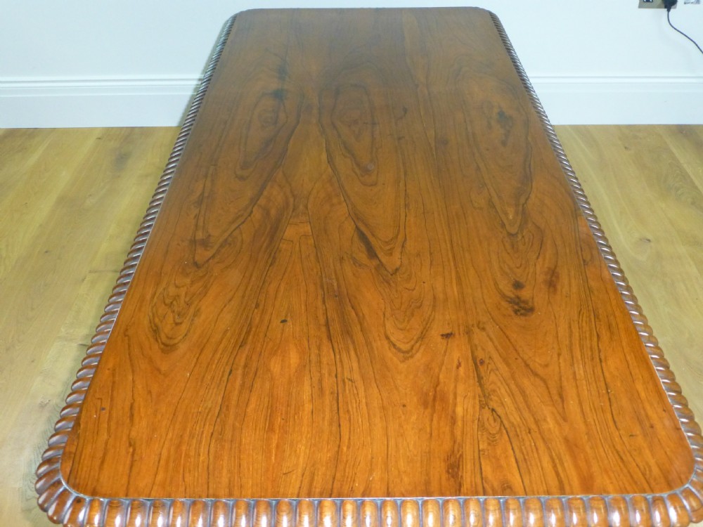 A Regency period rosewood writing table featuring a gadrooned top edge, frieze drawers, and carved trestle end supports. View VI