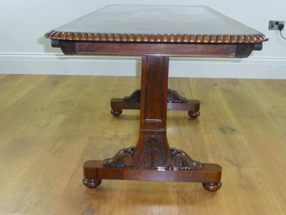 A Regency period rosewood writing table featuring a gadrooned top edge, frieze drawers, and carved trestle end supports. View VII