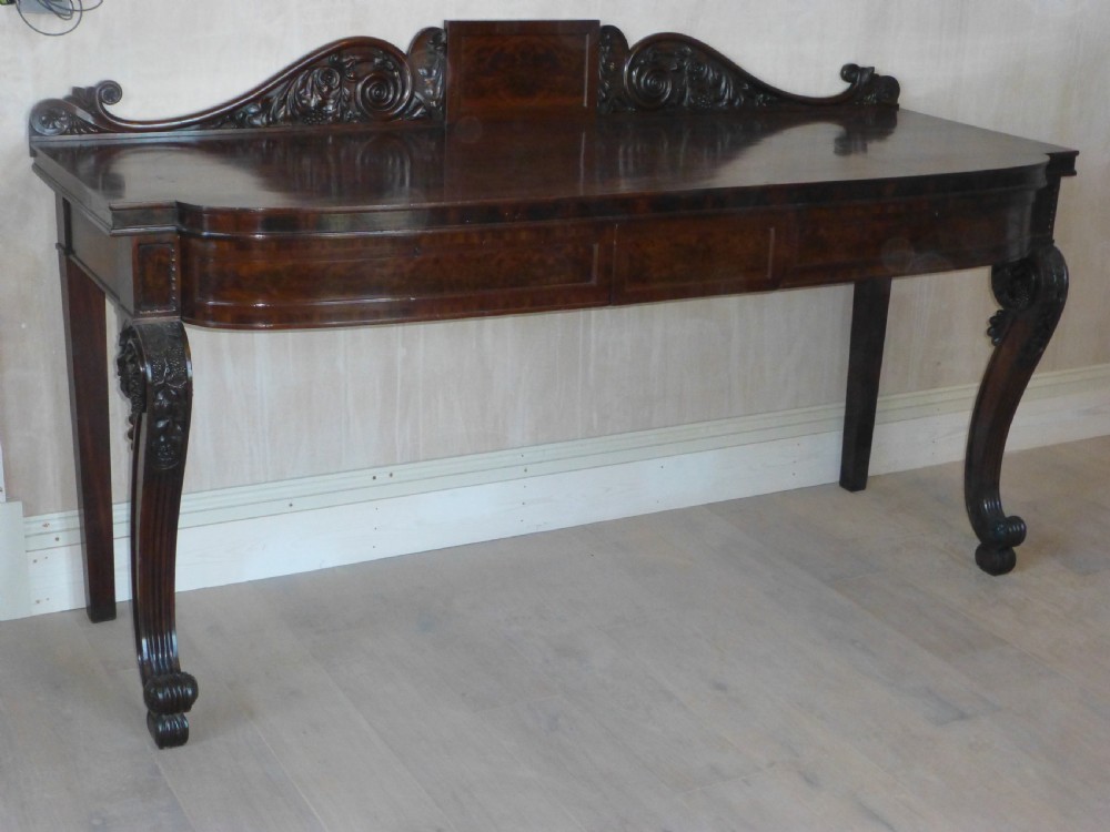 A dark mahogany Regency serving table featuring a scroll-carved backboard, a smooth top surface, and carved scroll front legs.