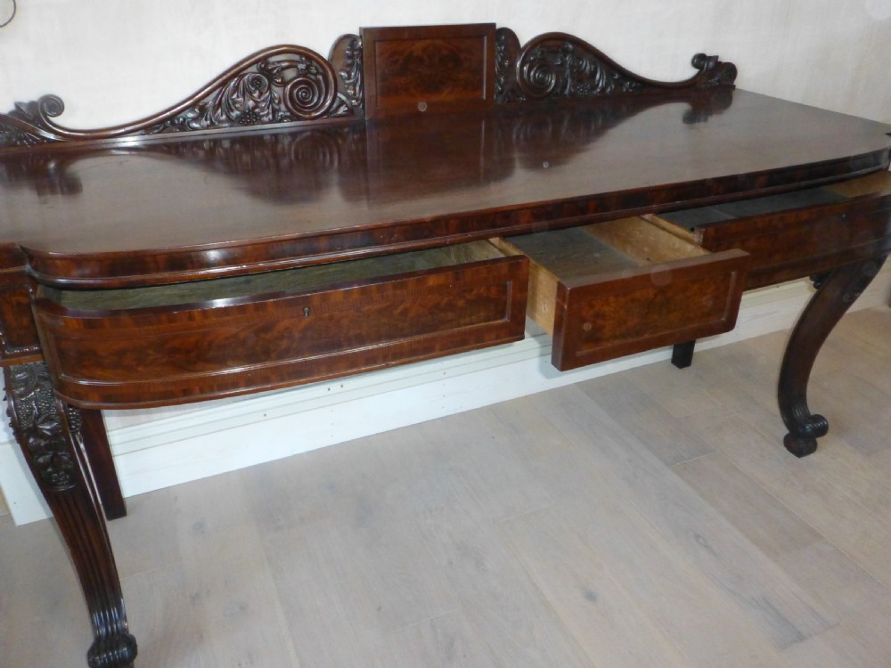A dark mahogany Regency serving table featuring a scroll-carved backboard, a smooth top surface, and carved scroll front legs. View XII
