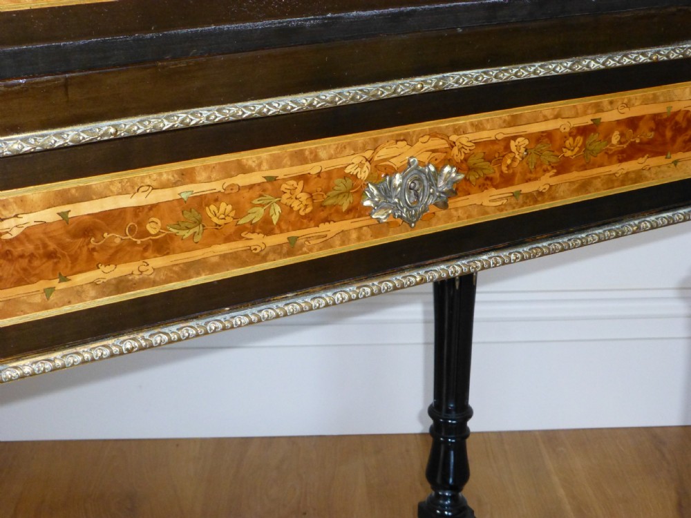 A nineteenth-century French slope-front writing desk featuring floral amboyna marquetry, ebonised turned legs with a shaped stretcher, and a brass gallery rail top. View V