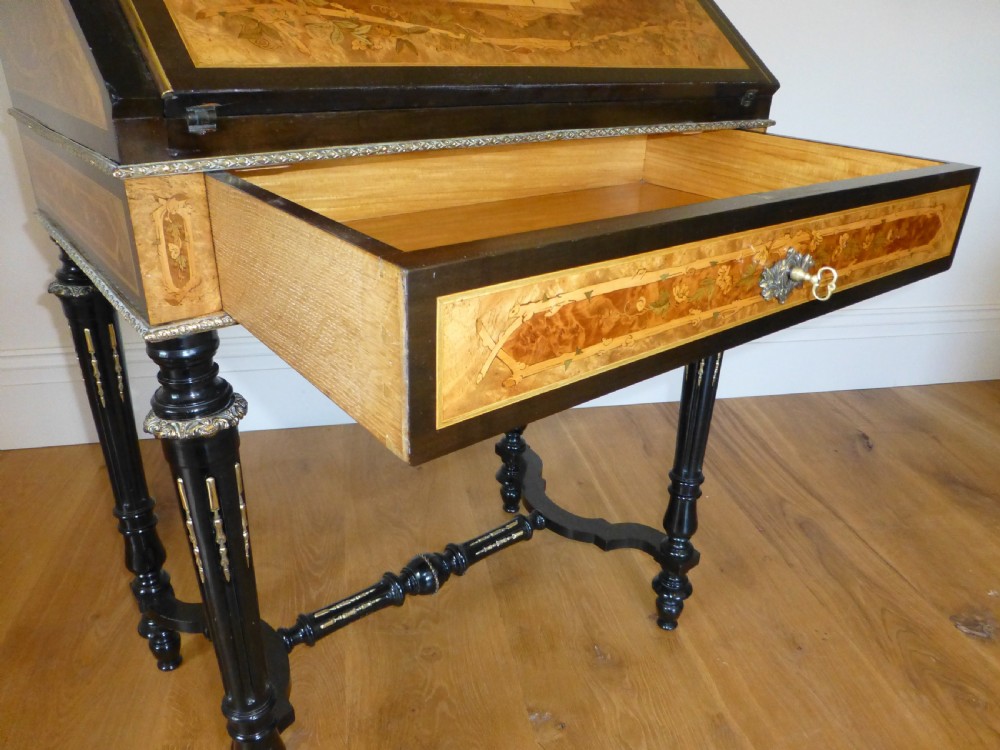 A nineteenth-century French slope-front writing desk featuring floral amboyna marquetry, ebonised turned legs with a shaped stretcher, and a brass gallery rail top. View VI