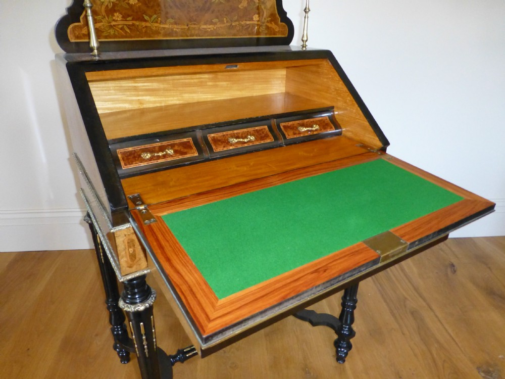 A nineteenth-century French slope-front writing desk featuring floral amboyna marquetry, ebonised turned legs with a shaped stretcher, and a brass gallery rail top. View VII